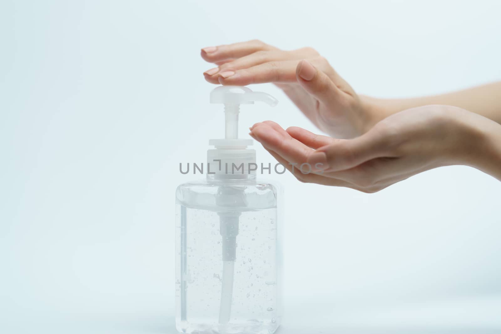Hand with hand sanitizer in a clear pump bottle on a white background.