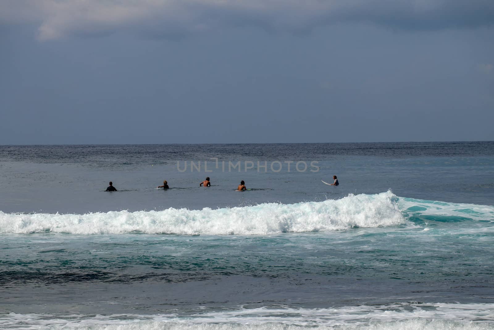 Unidentified man on surf board waiting for wave in blue water back view. Young Boys Waits the Waves. Surfer waiting in line for a wave. Surfers wait the wave in the sea during sunny tropical day.