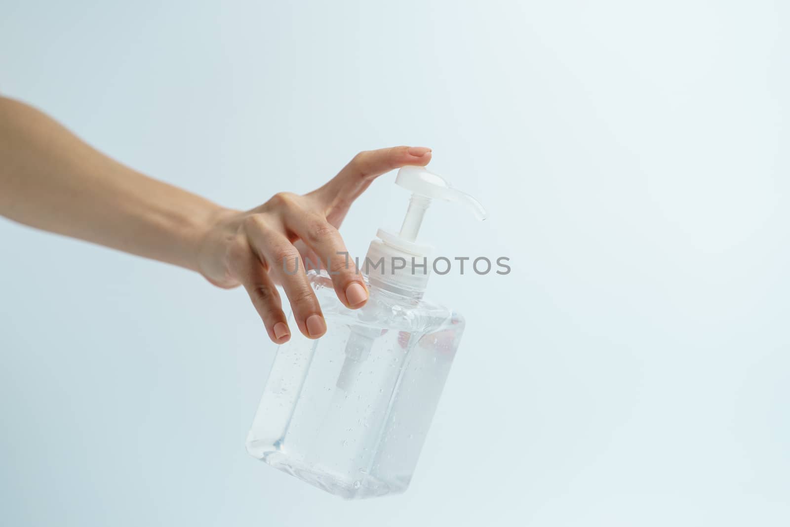 Hand with hand sanitizer in a clear pump bottle on a white background.