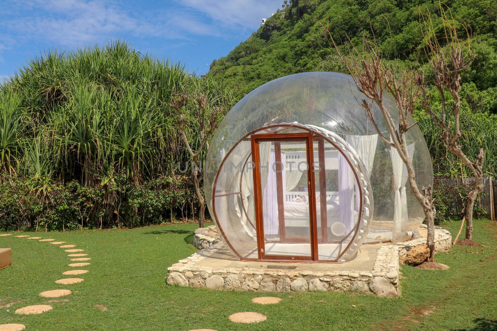 Romantic bubble hotel with transparent walls. White wooden double bed with mosquito net inside bubble house. Honeymoon in an inflatable tent. Tourist attraction in tropical paradise on Bali, Indonesia