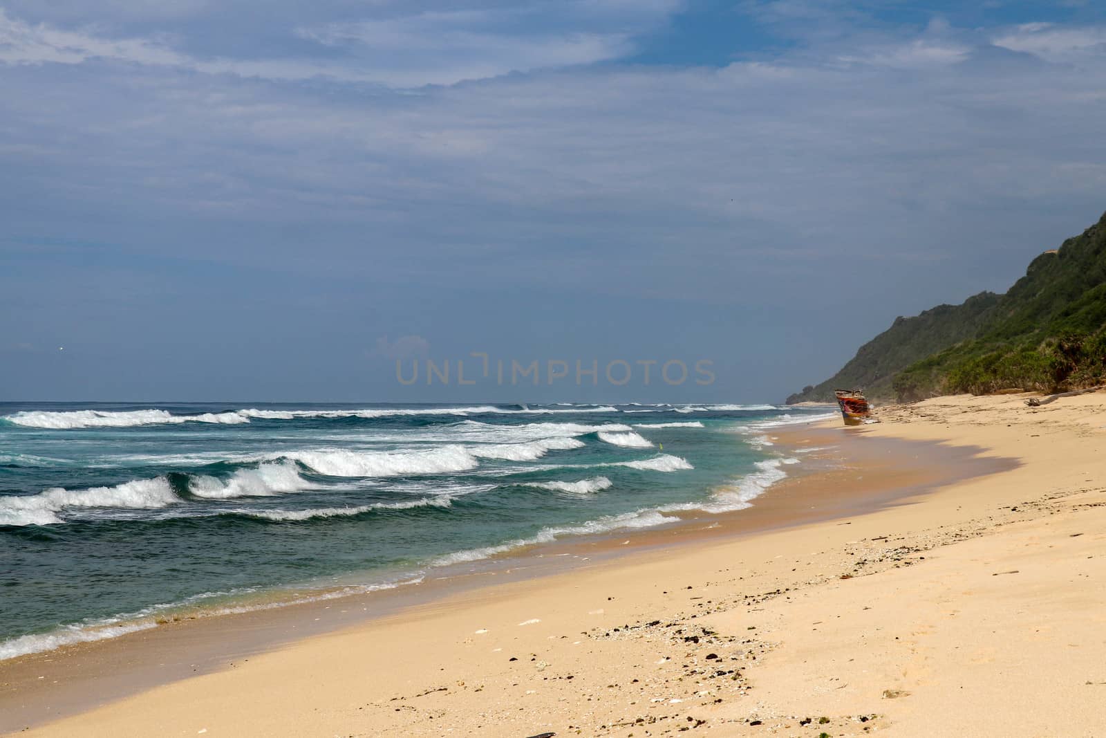 Virgin beach with fine yellow sand on Bali island. Tropical paradise with Nyang Nyang beach with high cliff on background. Wild waves are approaching the shore in rows. Sea foam in rolling waves.