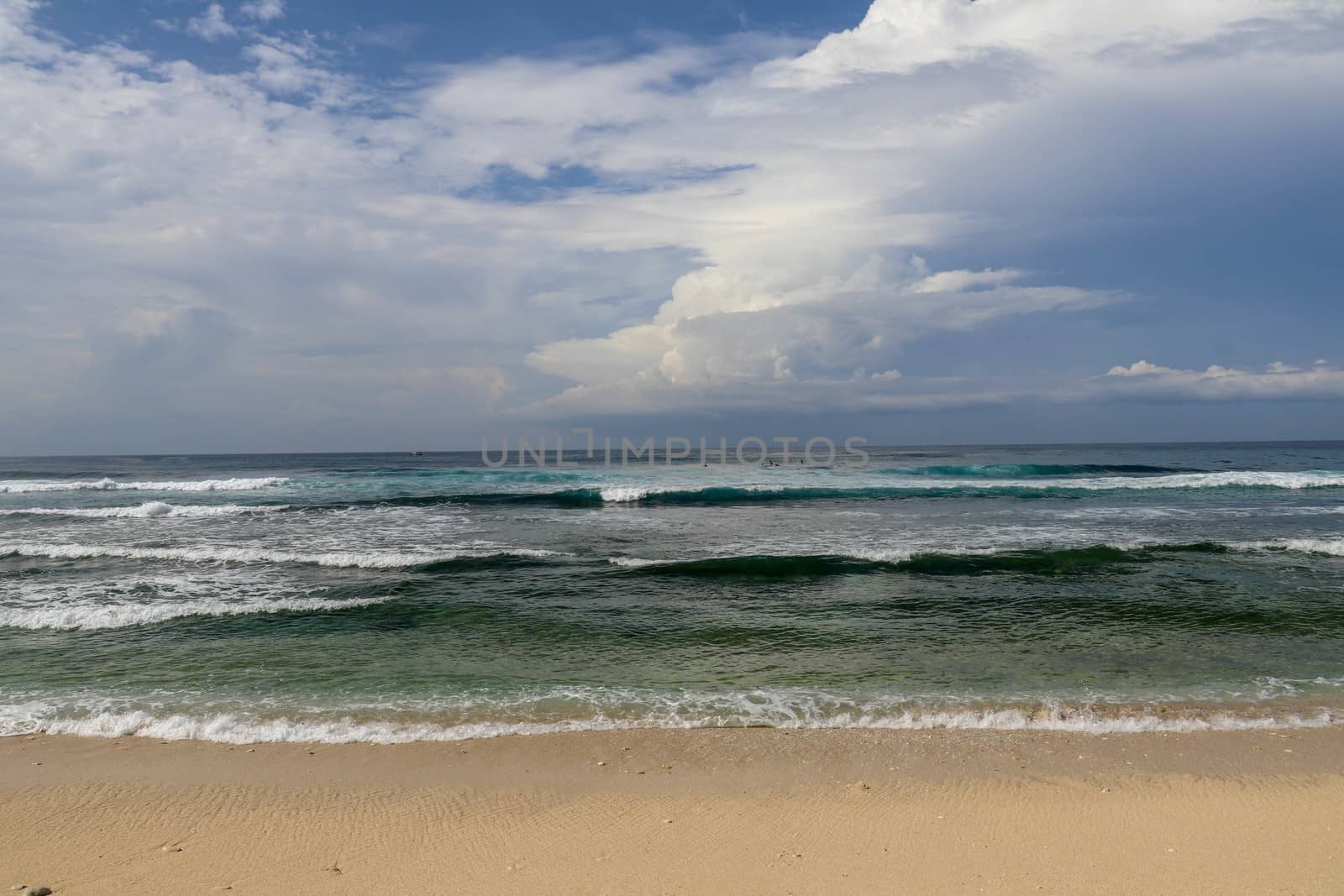 Surfers are waiting for a convenient wave on their surfboards. Tropical surfers paradise with Nyang Nyang beach on Bali island. Azure blue sky, sunny day. Wild waves are approaching the shore in rows.