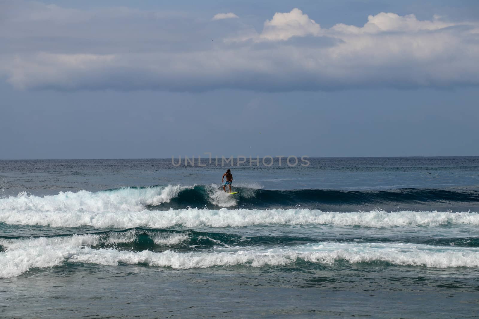 Young man sliding down a wave on a yellow surfboard. Surfer on a yellow surfboard on the crest of the wave. Young surfer learns to catch waves. First steps in surfing sport.