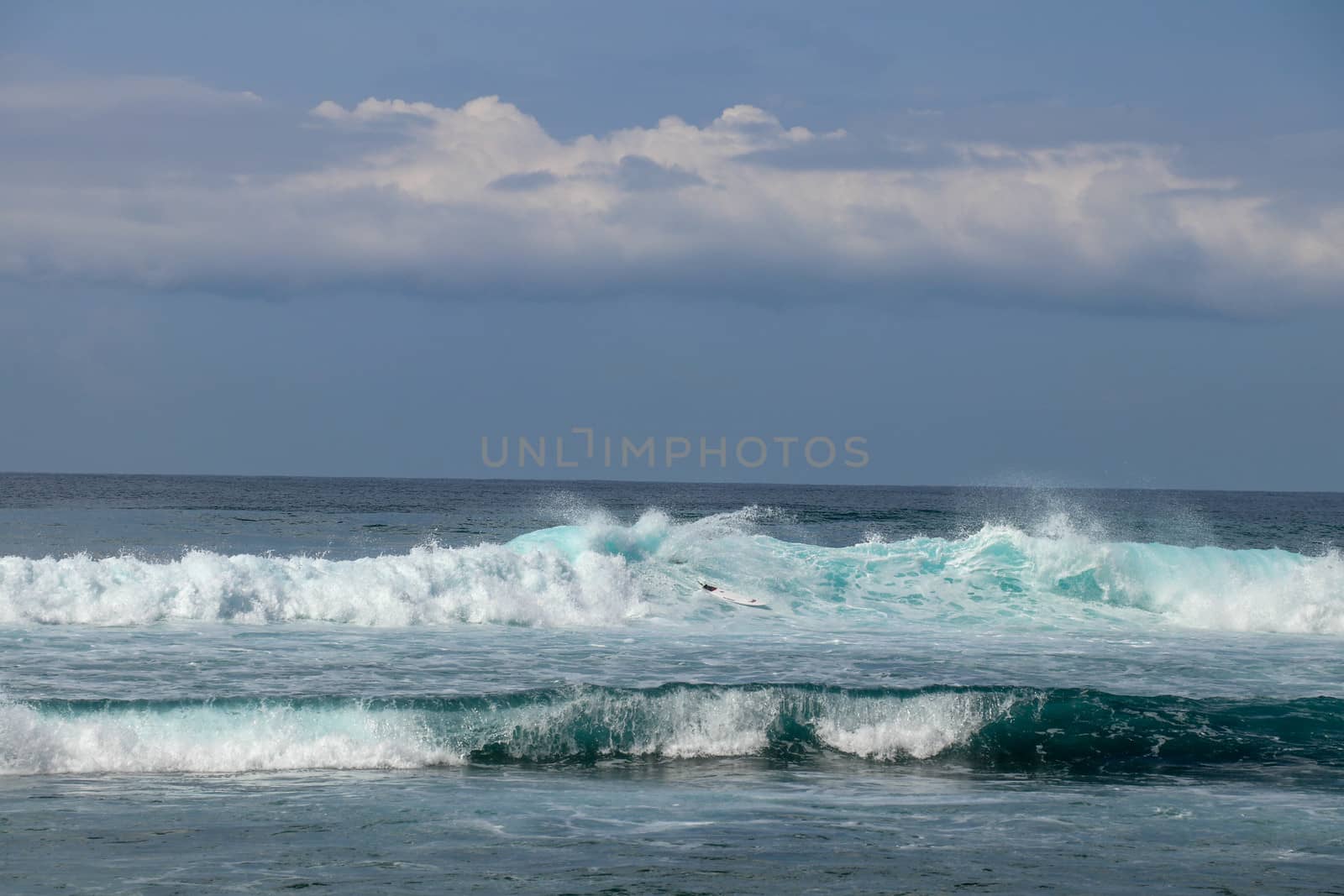 Young caucasian man surfs the ocean wave and makes a lot of splashes into the camera. Nyang Nyang Surf Spot in Bali, Indonesia. The surfer falls into the ocean waves. Man rides the wave at sunny day.