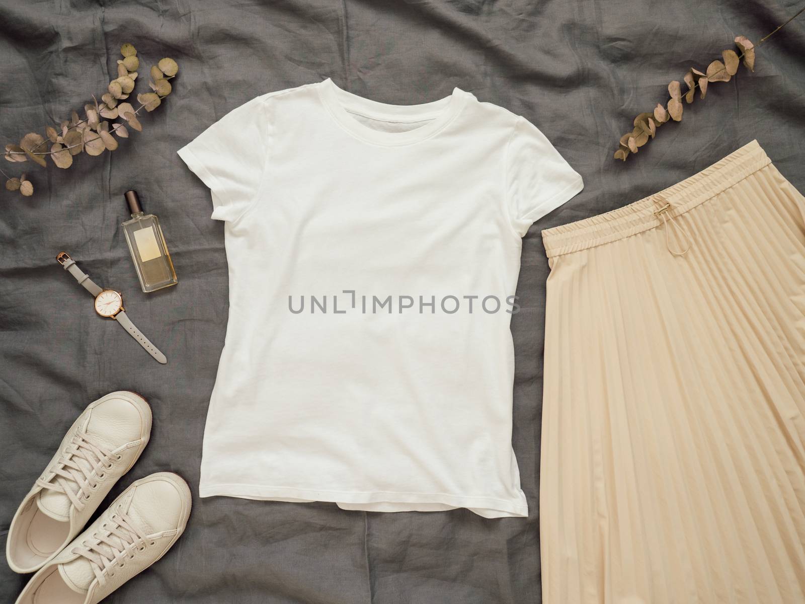 Fashionable female look with white empty t-shirt, cream pleated skirt and white sneakers. Top view of white blank t-shirt with short sleeves over gray bed linen. Mock up for t-shirt print design.