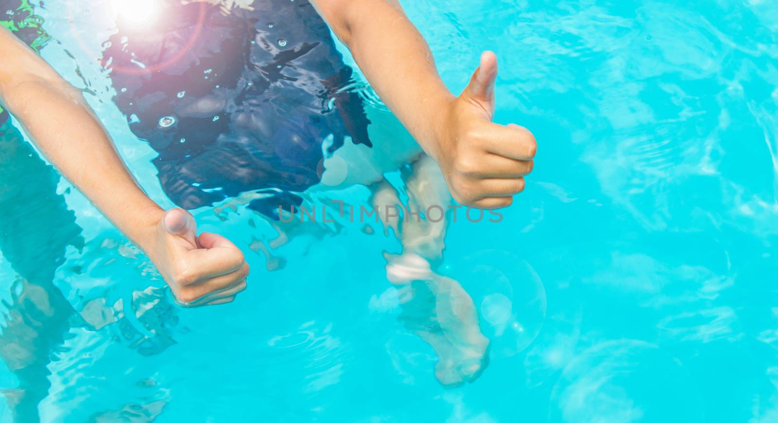 Thumbs up two teenage girls with long hair in swimsuits in a pool with blue sparkling water in the open, sunlight, glare summer.