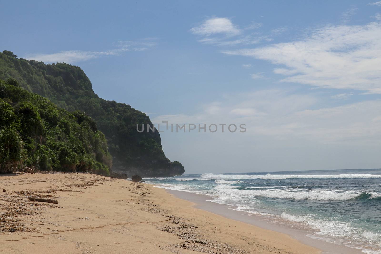 Virgin beach with fine yellow sand on Bali island. Tropical paradise with Nyang Nyang beach with high cliff on background. Wild waves are approaching the shore in rows. Sea foam in rolling waves.