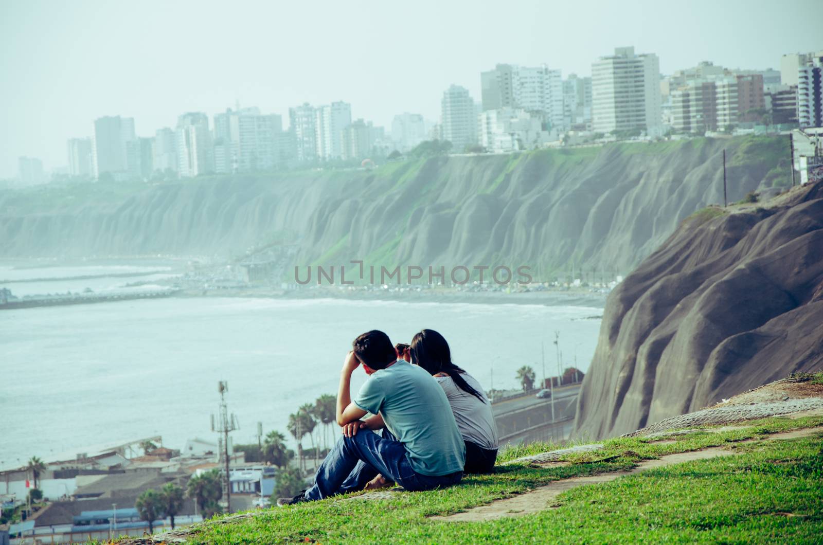 A couple sitting on the edge of the cliff on the coast of Lima - Peru facing the sea