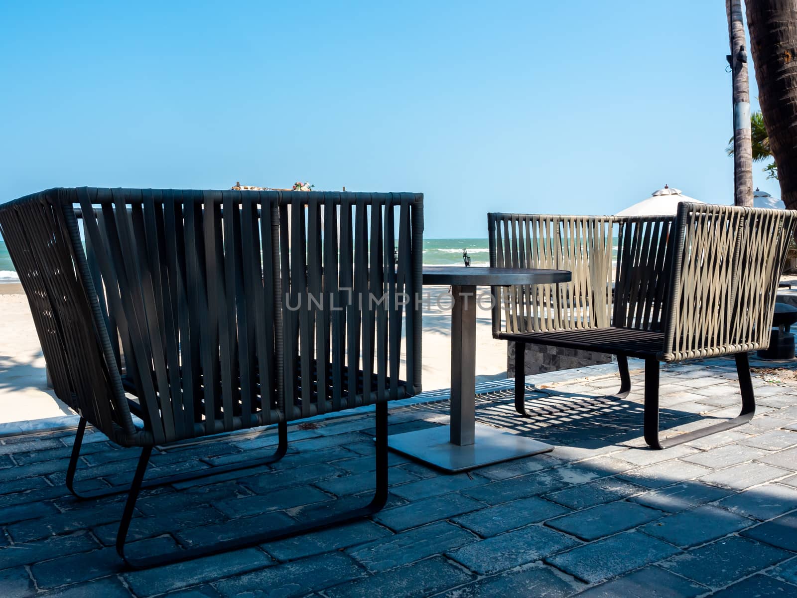 Modern chairs with round side table on balcony with sea view near the beach on blue sky background.
