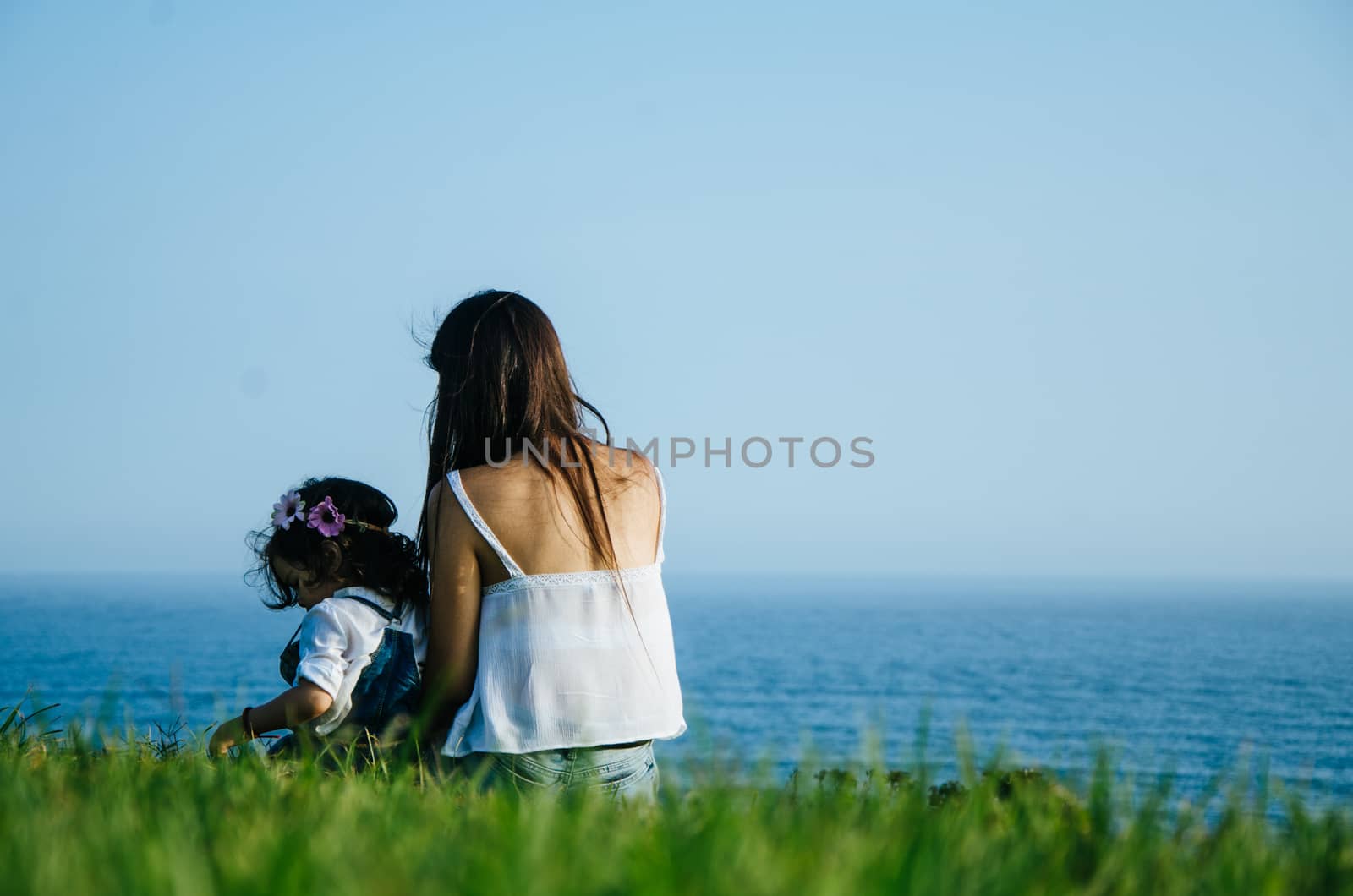 Mother and daughter sitting on the lawn facing the sea