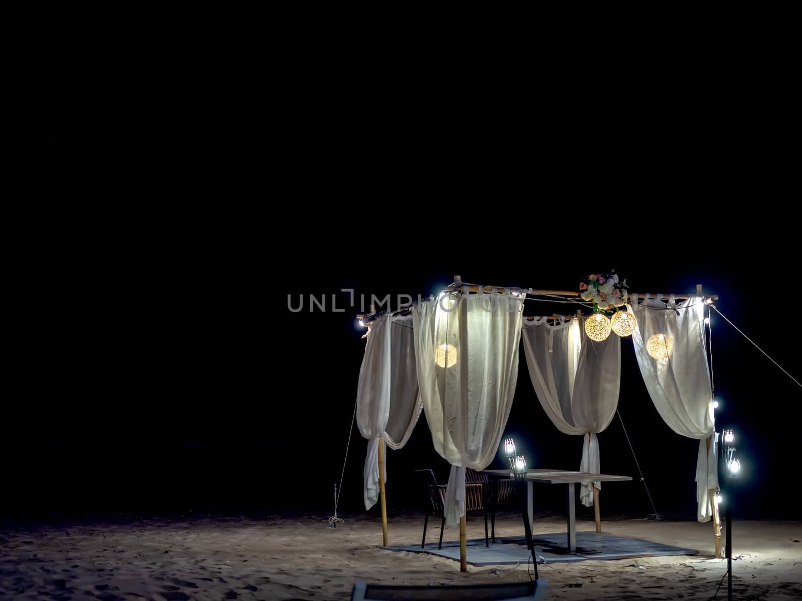 Romantic dining table, ornament with wood, lamp and white fabric on the beach at night on dark background.