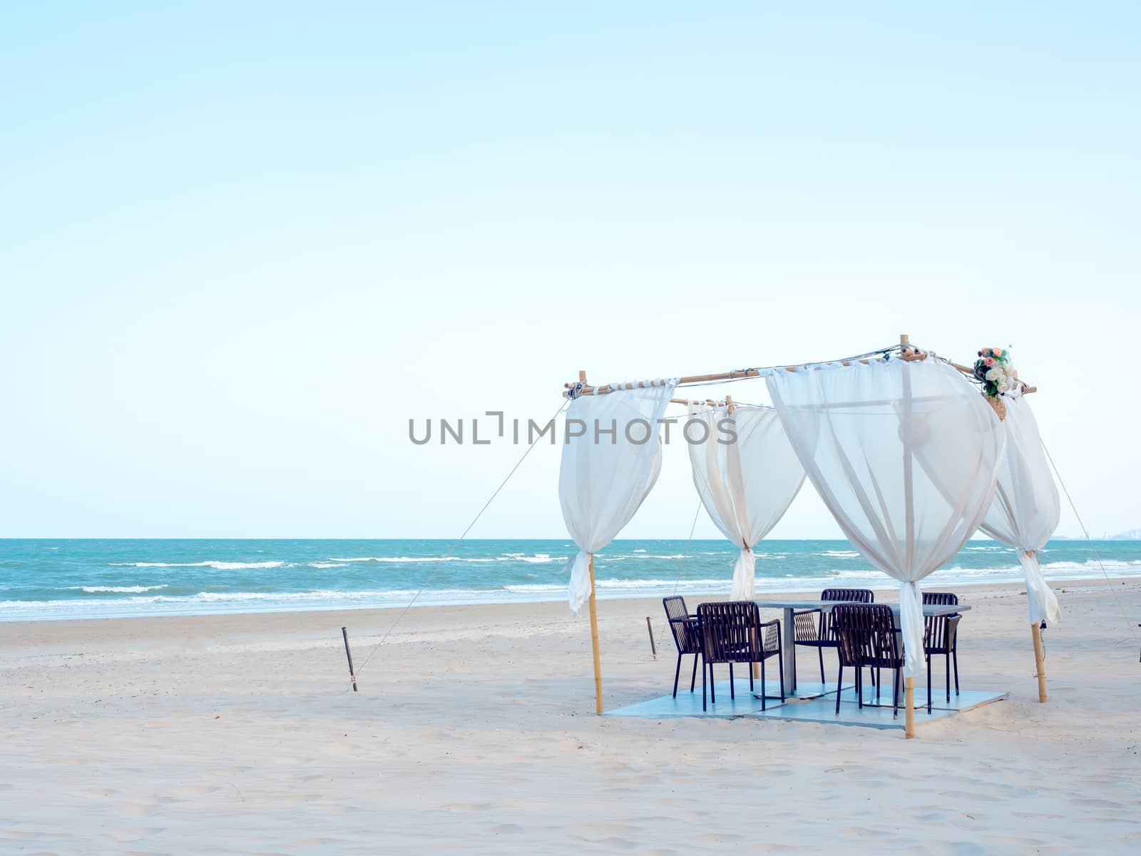 Romantic dining table, ornament with wood and white fabric on the beach on soft blue sky background.