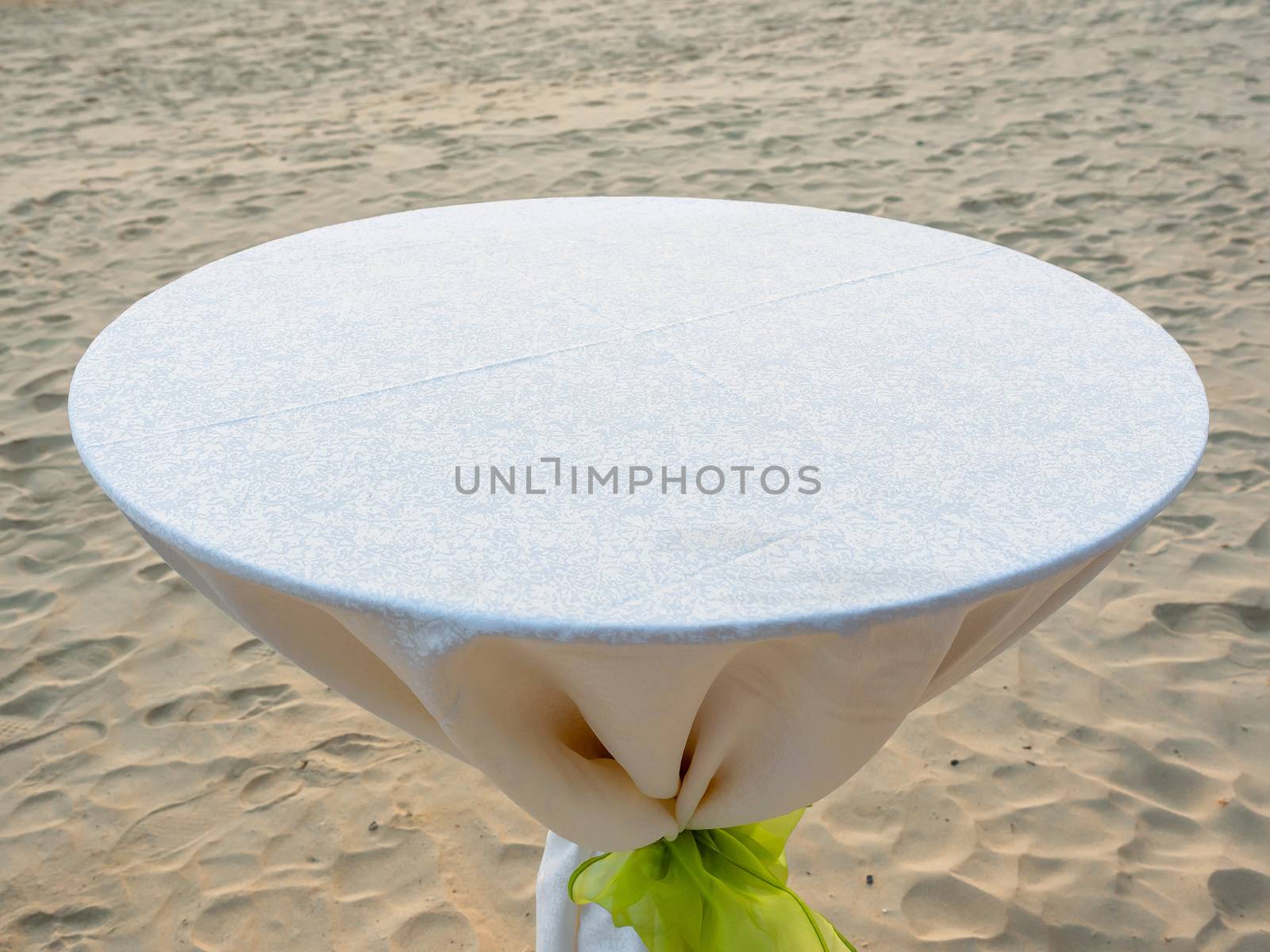 Empty round dining table with white tablecloth and light green bow on the beach.
