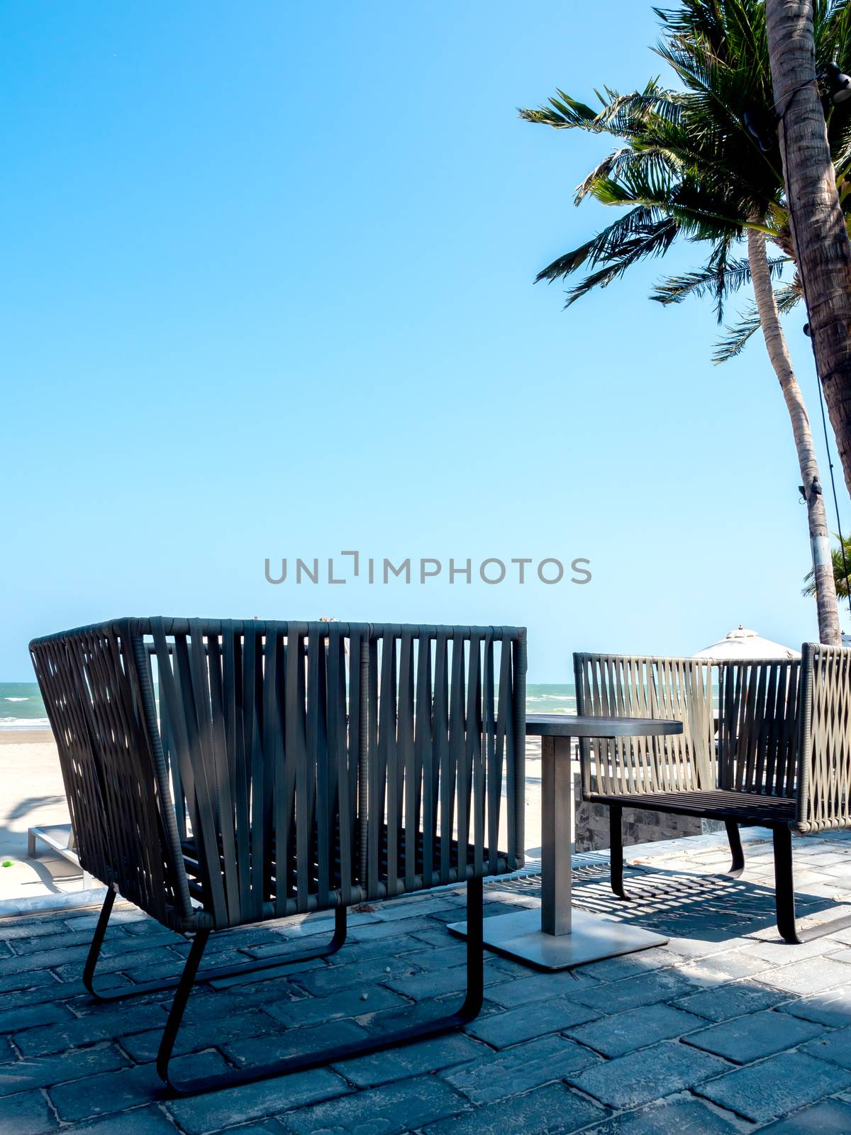 Modern chairs with round side table on balcony with sea view near the beach on blue sky background, vertical style.