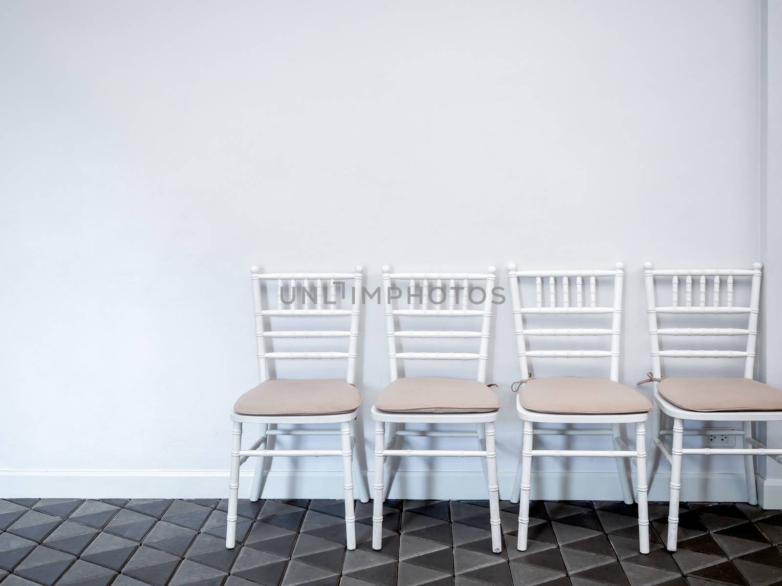 Row of clean white vintage wooden chairs with pads on modern stone tiles floor on white wall background with copy space.