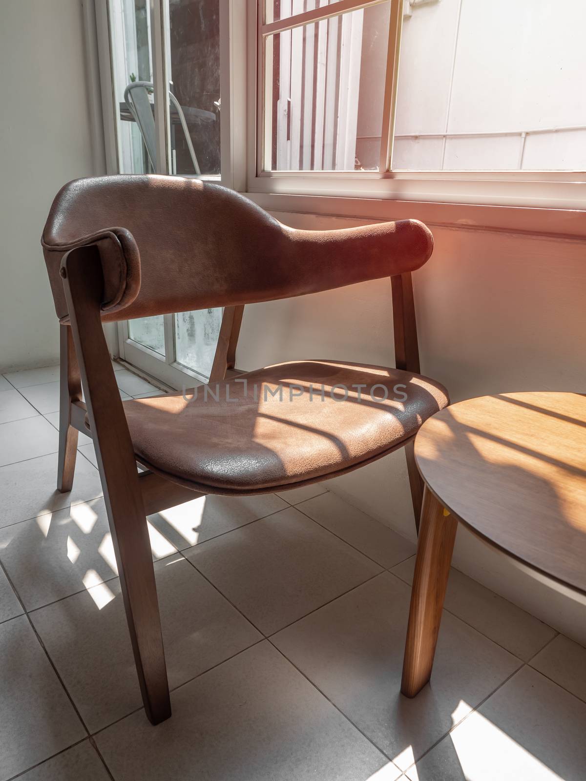 Wooden armchair retro style with brown leather seat pad and wooden table near the window in white room, vertical style.