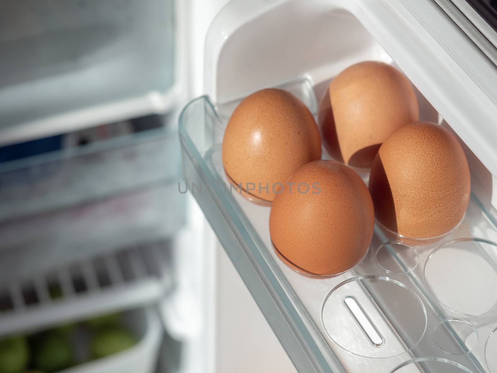 Four fresh chicken eggs on shelf of white refrigerator.