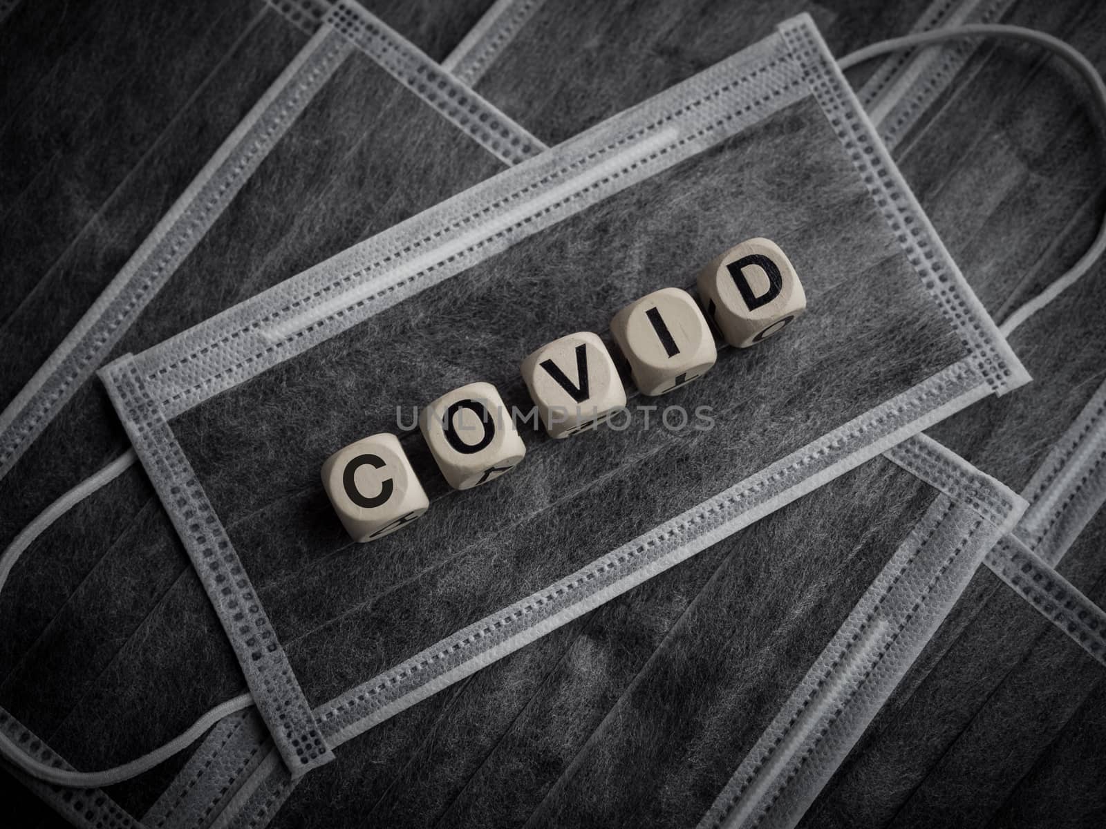 Coronavirus or Covid-19 concept. Wooden cubes text "COVID" on many protective face masks background.