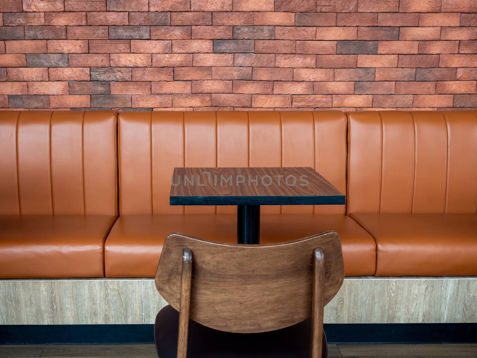 Furniture decoration in cafe retro style. Empty wood table bar and orange long leather sofa and wooden chair on brick wall background.