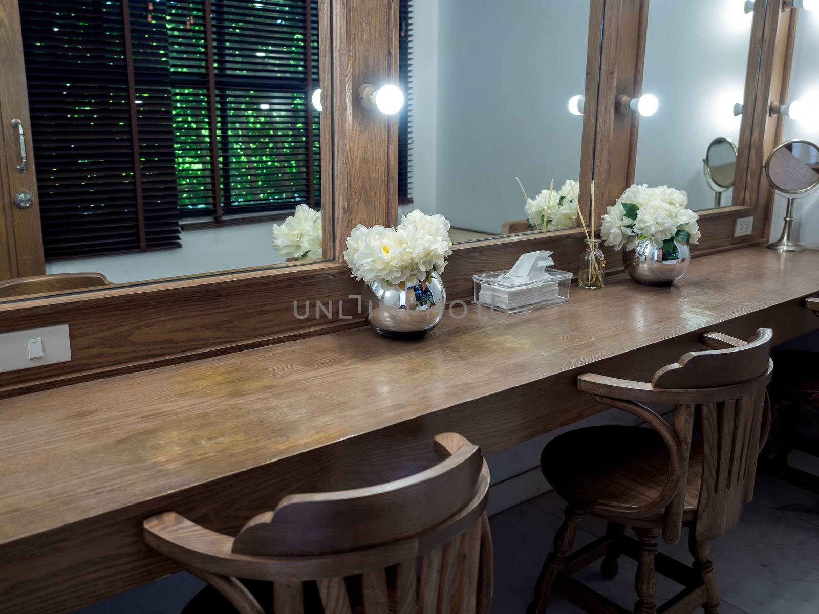 Makeup room classic and vintage style decoration with long wooden table, wooden chairs, mirrors with light bulbs and modern flower pot.