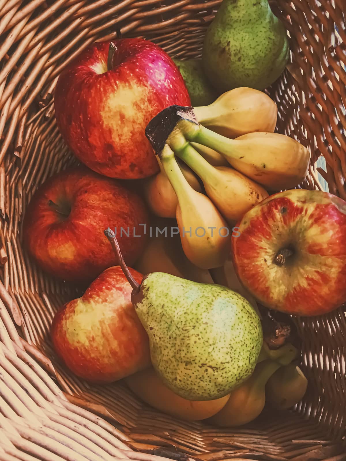 Organic apples, pears and bananas on rustic in a wicker basket by Anneleven