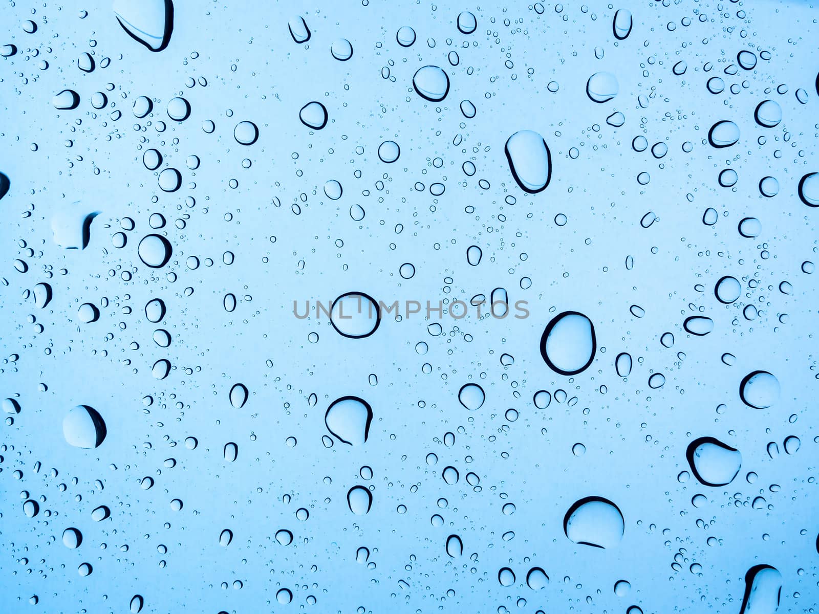 Water droplet on glass background. Light blue water drops texture on windshield on rainy day.