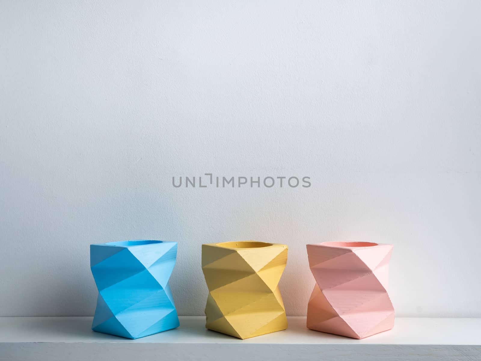 Cactus pot. Concrete pot. Three empty blue, pink and yellow modern geometric concrete planters on white wooden shelf isolated on white background.