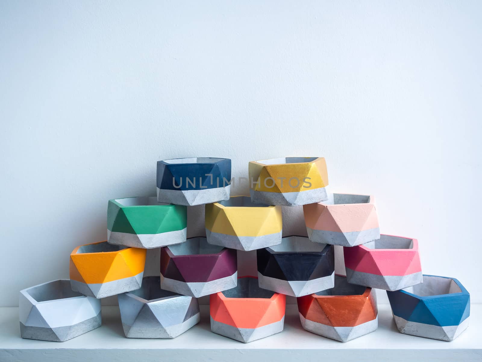 Cactus pot. Concrete pot. Pyramid pile of empty colorful pentagon concrete planters on white wooden shelf isolated on white background.