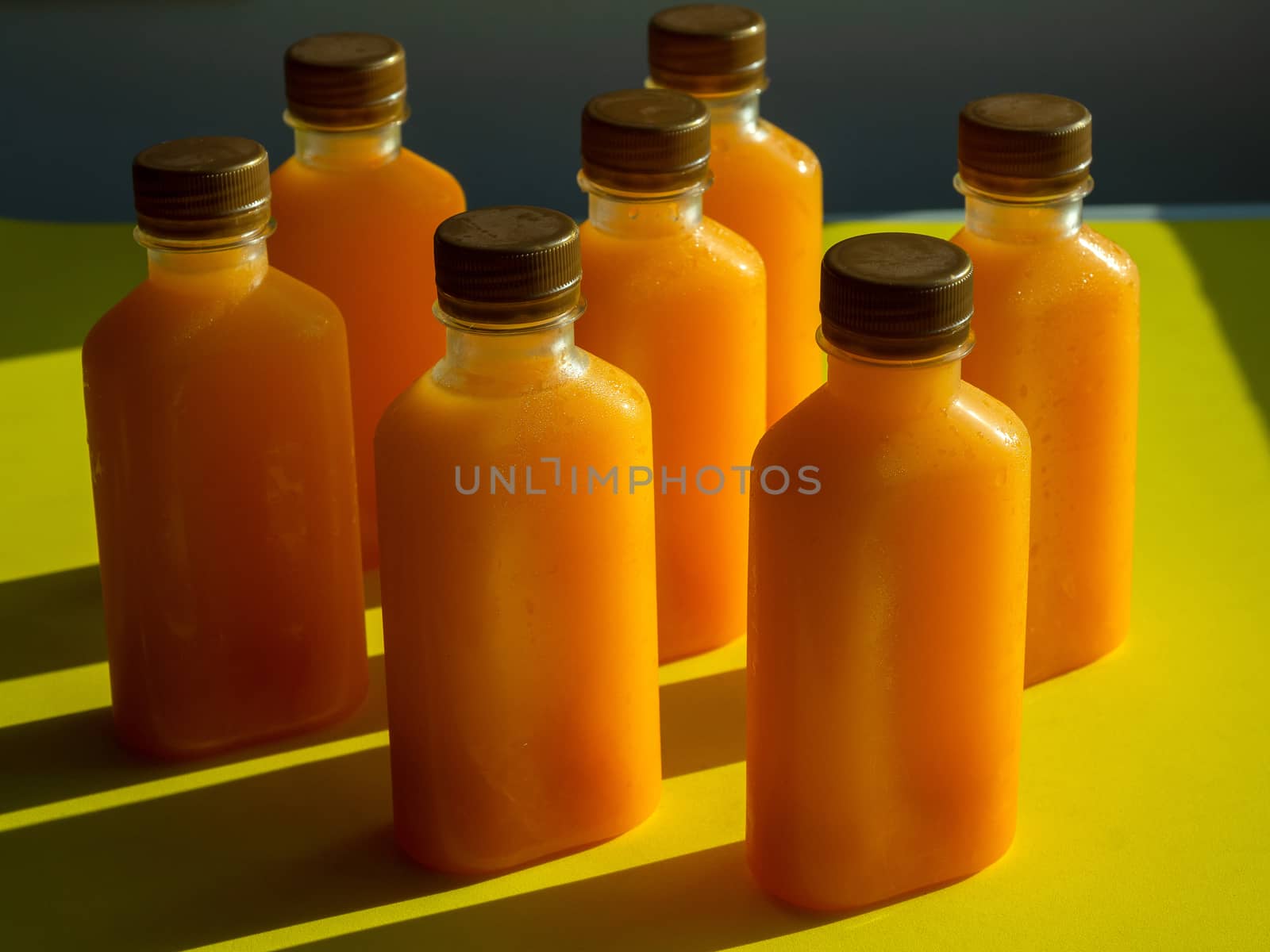 Orange juice iced cold in the bottles. Close-up square shape bottle with cold orange juice on yellow background minimalist style.