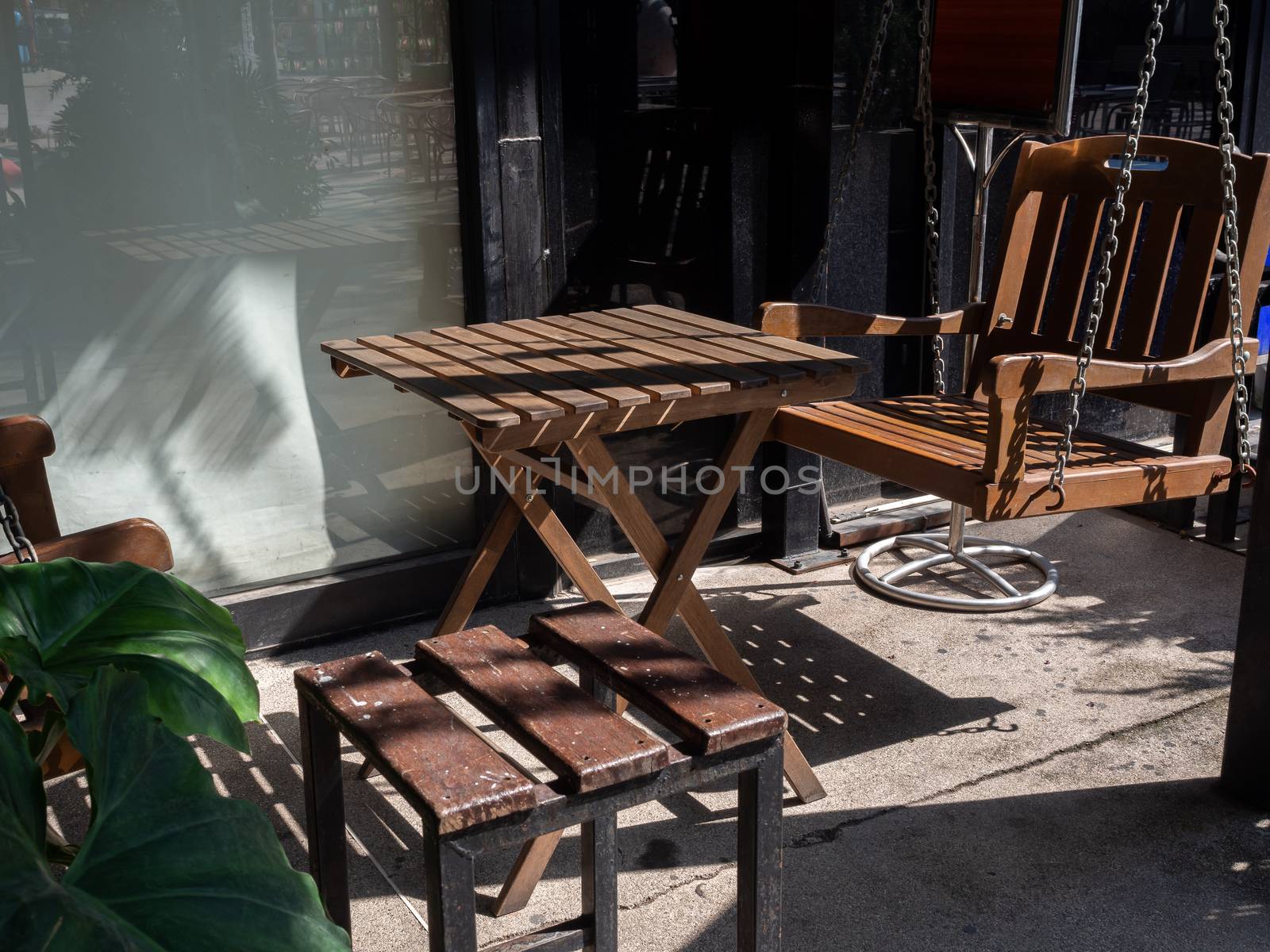 Wooden table, wooden chair and wooden swing in the backyard. Shady place for relaxation.