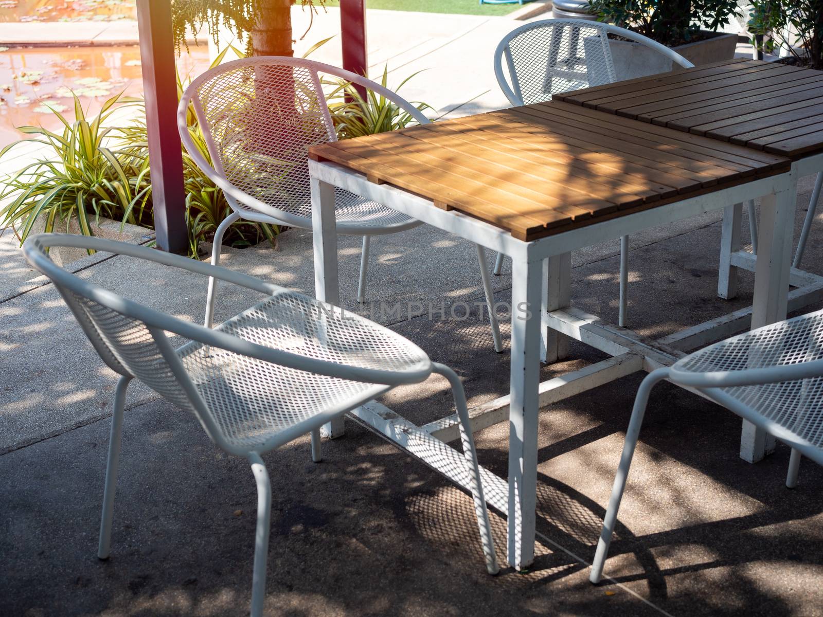 Wooden table and white retro style armchair in terrace. Shady place for relaxation.
