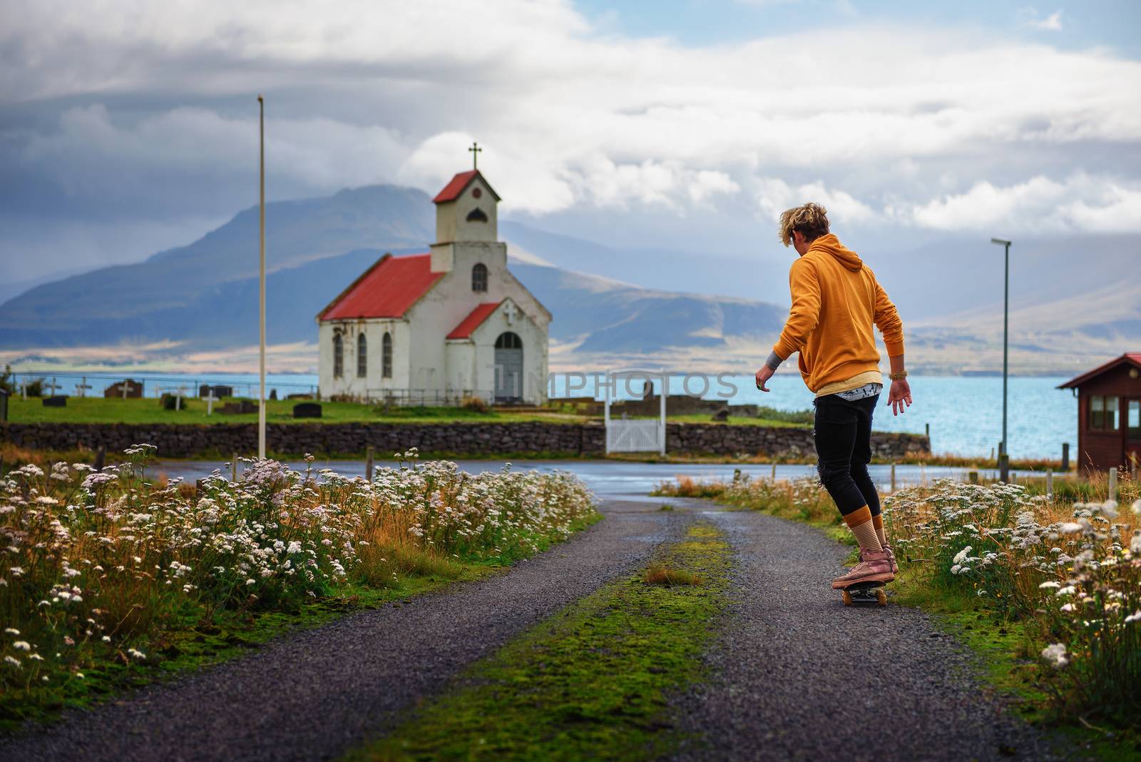 Young skater skateboarding towards a church and a cemetery in Iceland by nickfox