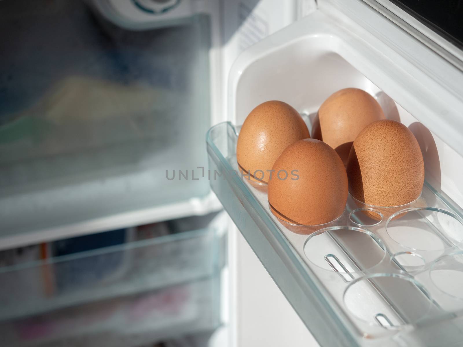 Four fresh chicken eggs on shelf of white refrigerator with copy space.