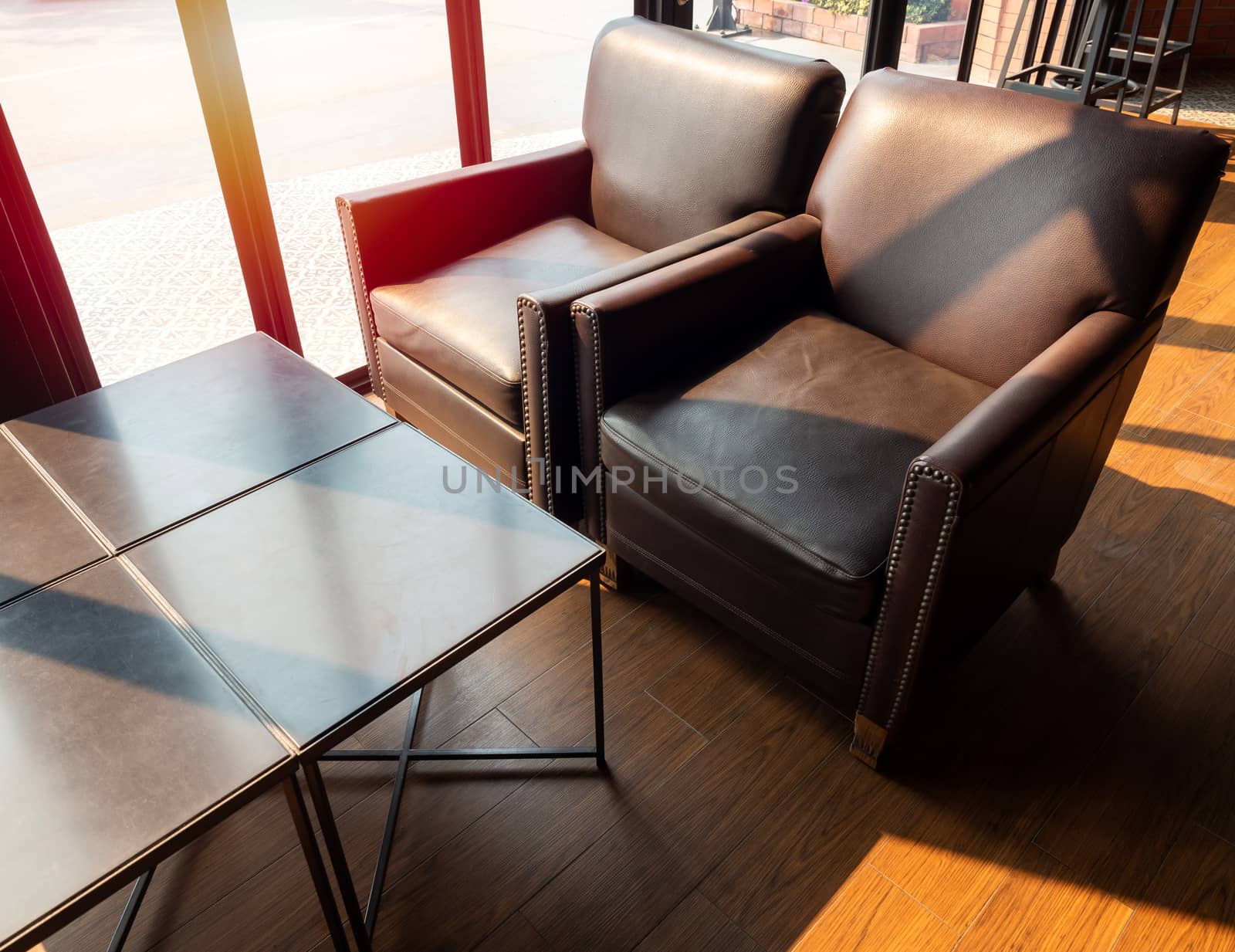 Brown leather sofa with wooden table on wooden floor near glass window in cafe on sunshine day.