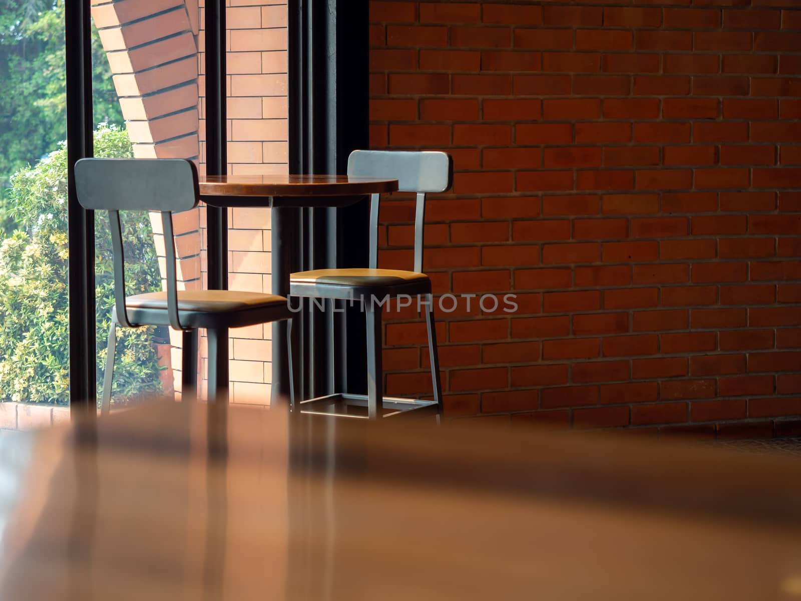 Cafe decoration design. Round wooden table with two modern bar stools on wooden floor near the glass window near brick wall on sunshine day with copy space.