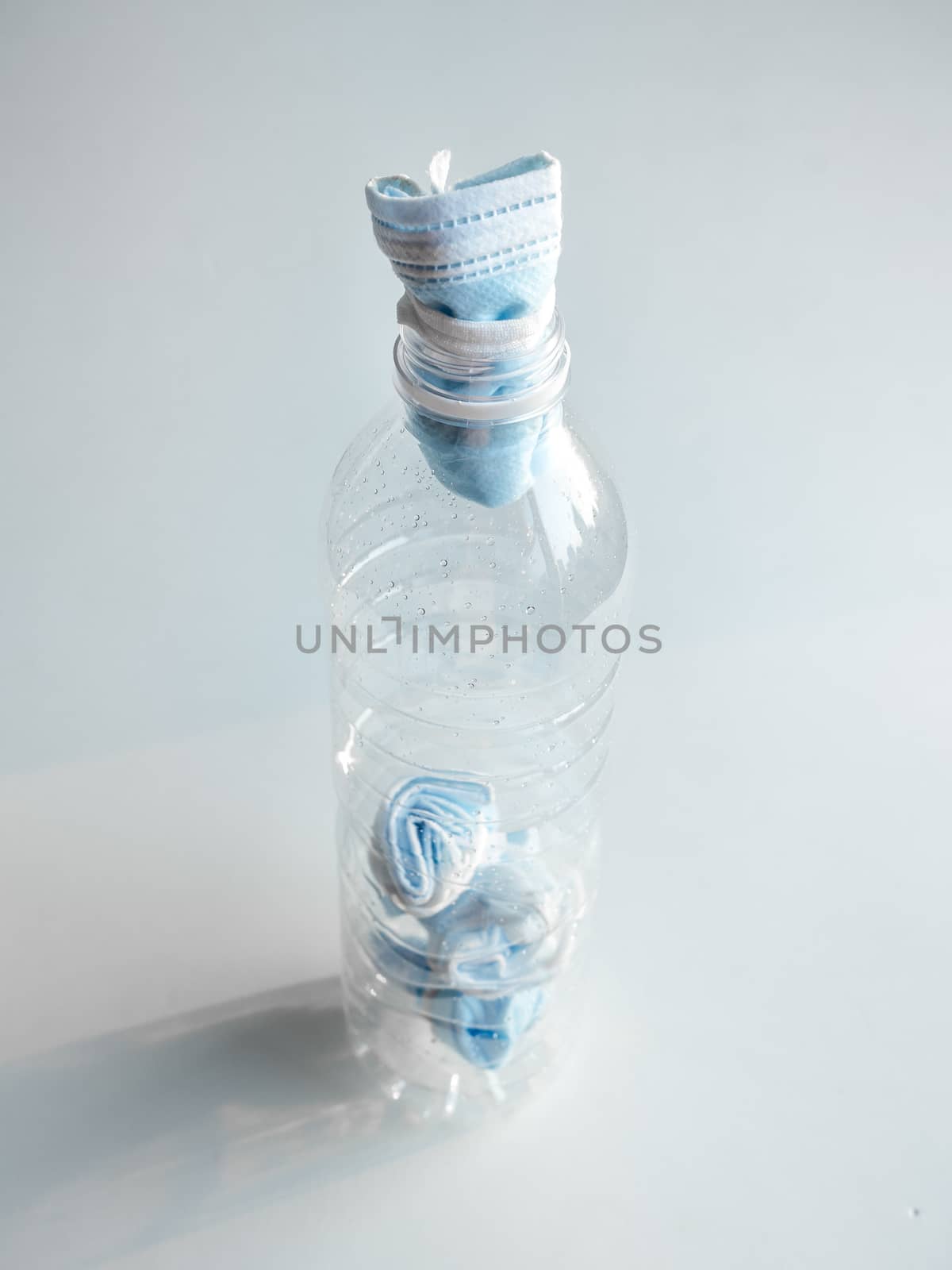 Used mask concept. Folded used protective face mask in plastic bottle on white background vertical style. Protection before littering for prevent spread of virus.