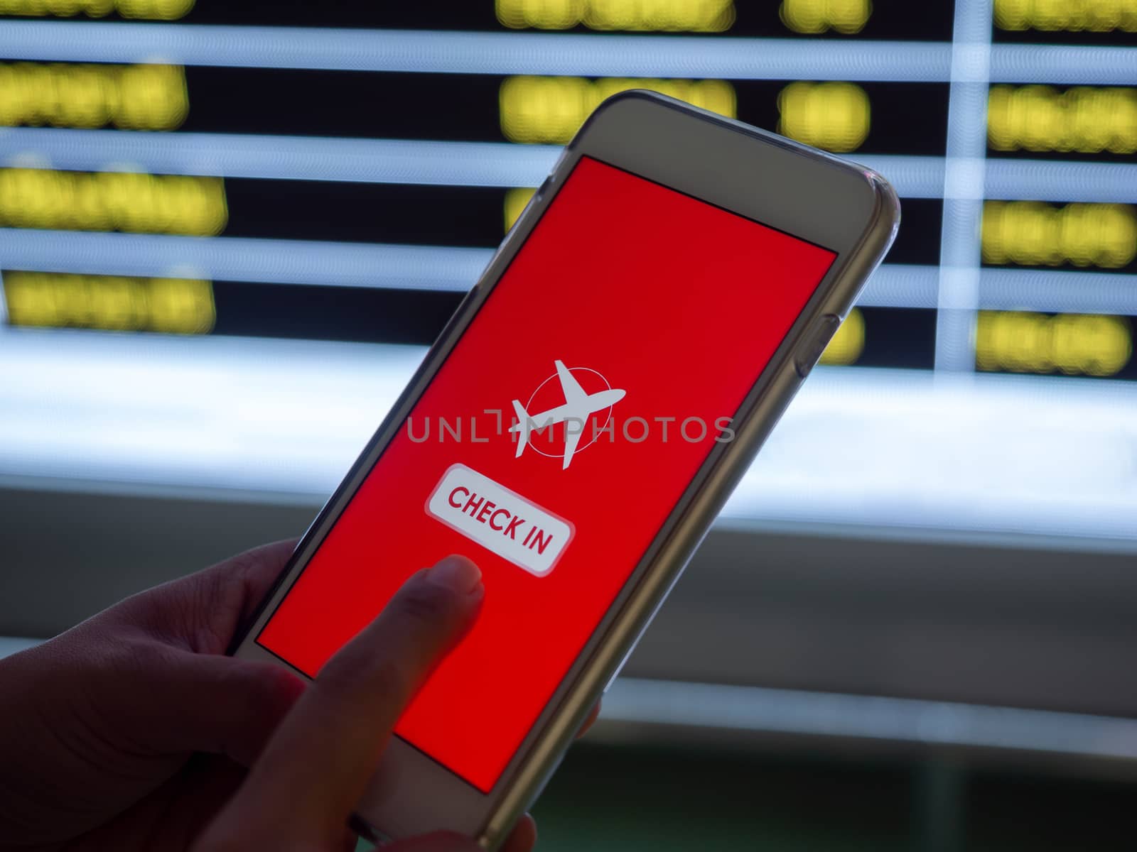 Flight check-in by mobile phone. Hand touching on smartphone screen to check-in for a flight in front of flight schedule board information background in airport.