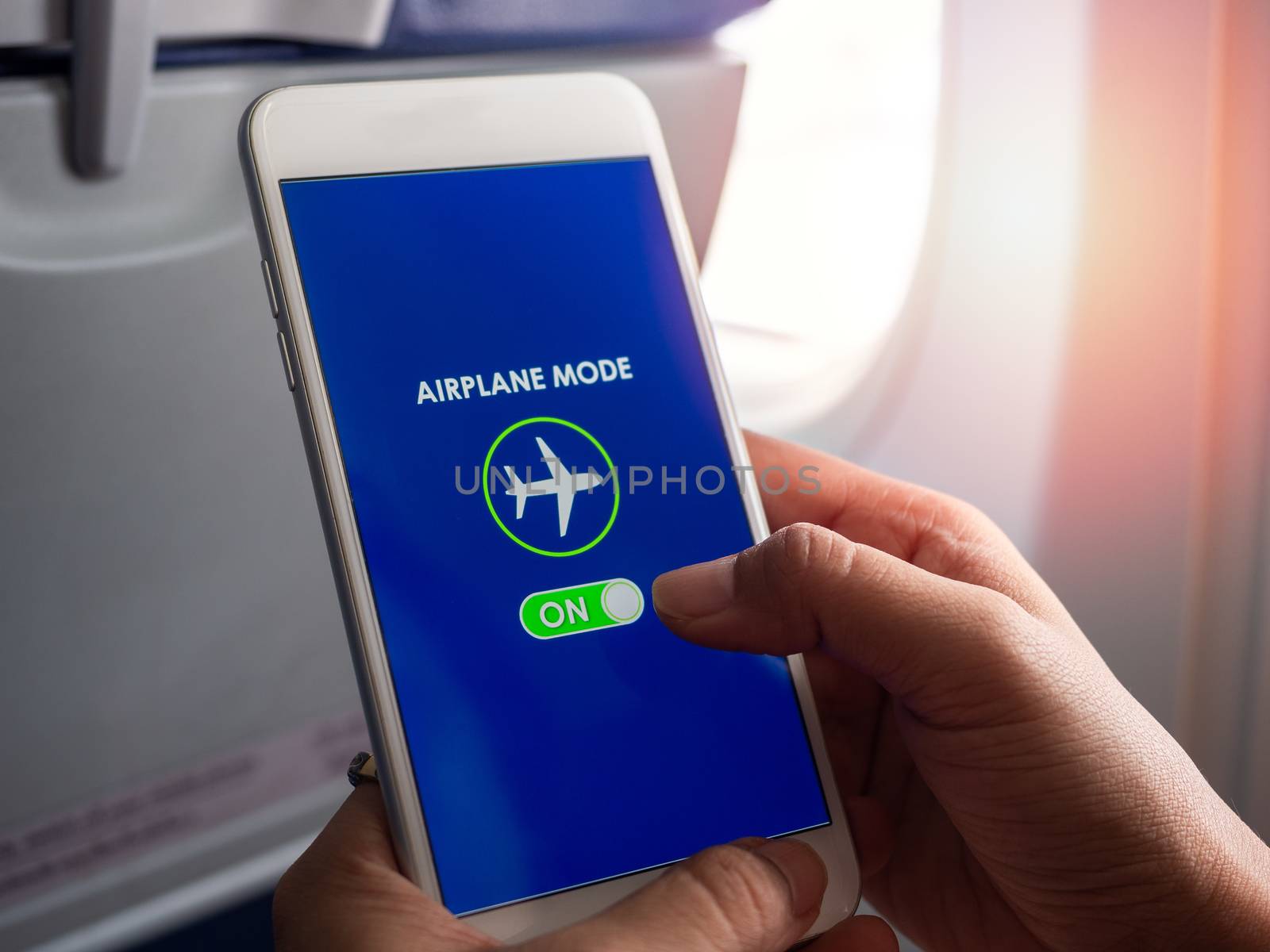 Flight mode concept. Close-up finger sliding on screen for turned on airplane mode near the window on the airplane.