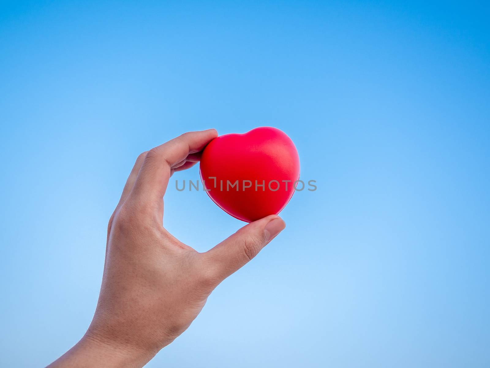 Red heart in hand on blue sky background, love, peace and giving concept.