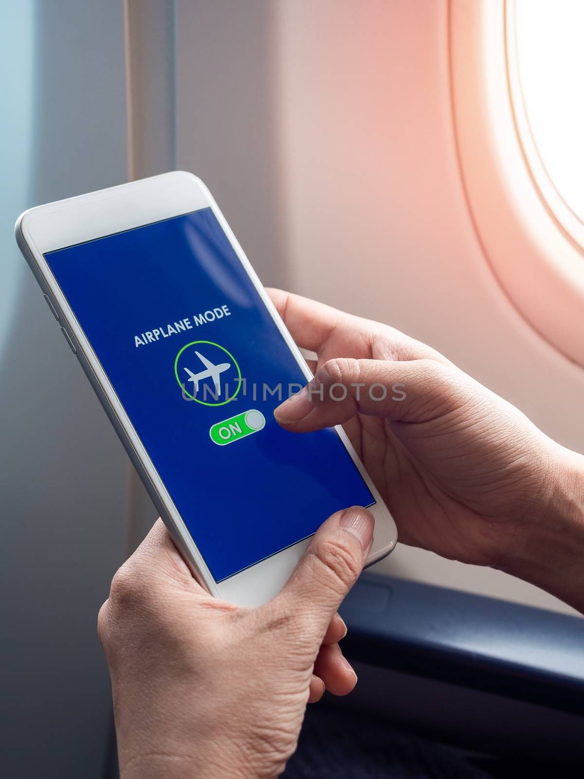 Flight mode concept. Hand holding white smartphone and turned on airplane mode on screen near the window on the airplane vertical style.