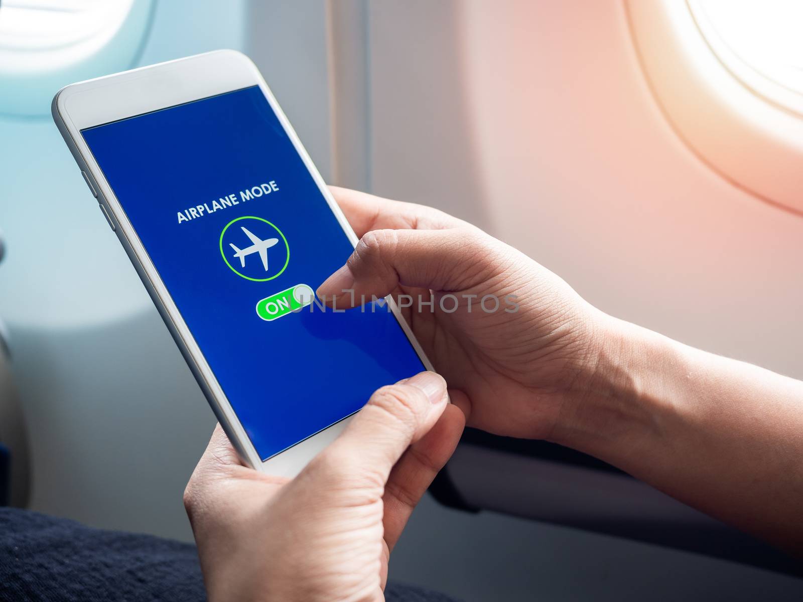 Flight mode concept. Finger sliding on screen for turned on airplane mode near the window on the airplane.