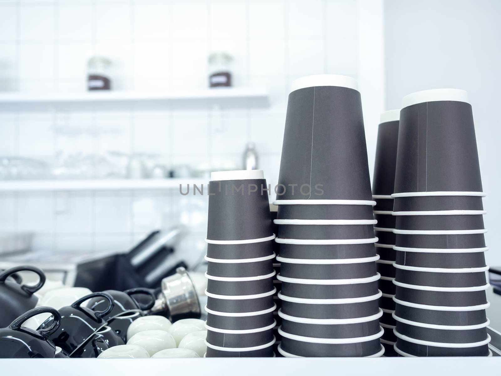 Black paper coffee cups stacked in a pile. Row of black paper cups upside down on shelf on white cafe background with copy space.