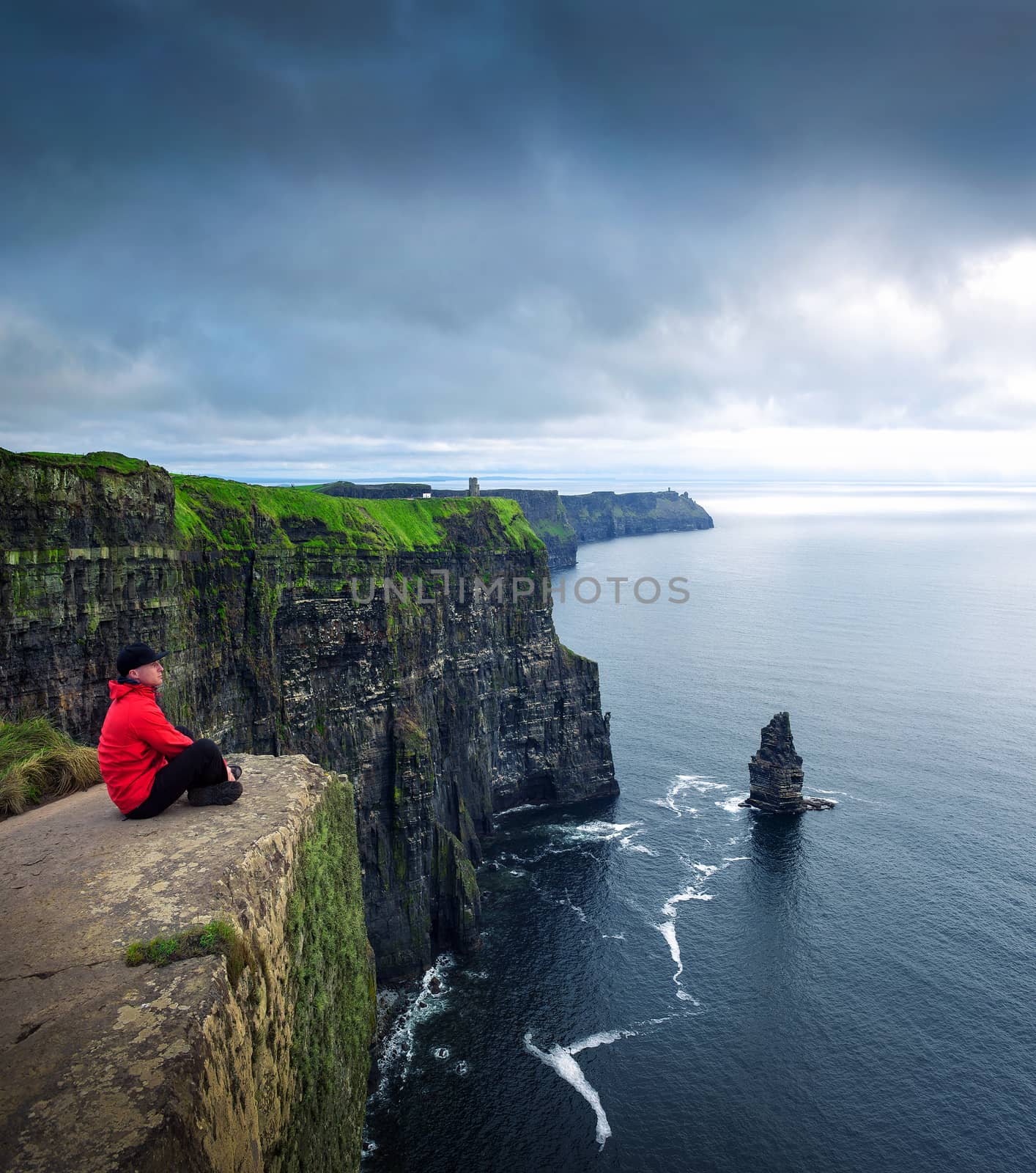 Hiker sitting at the cliffs of Moher located at the edge of the Burren region in County Clare, Ireland.