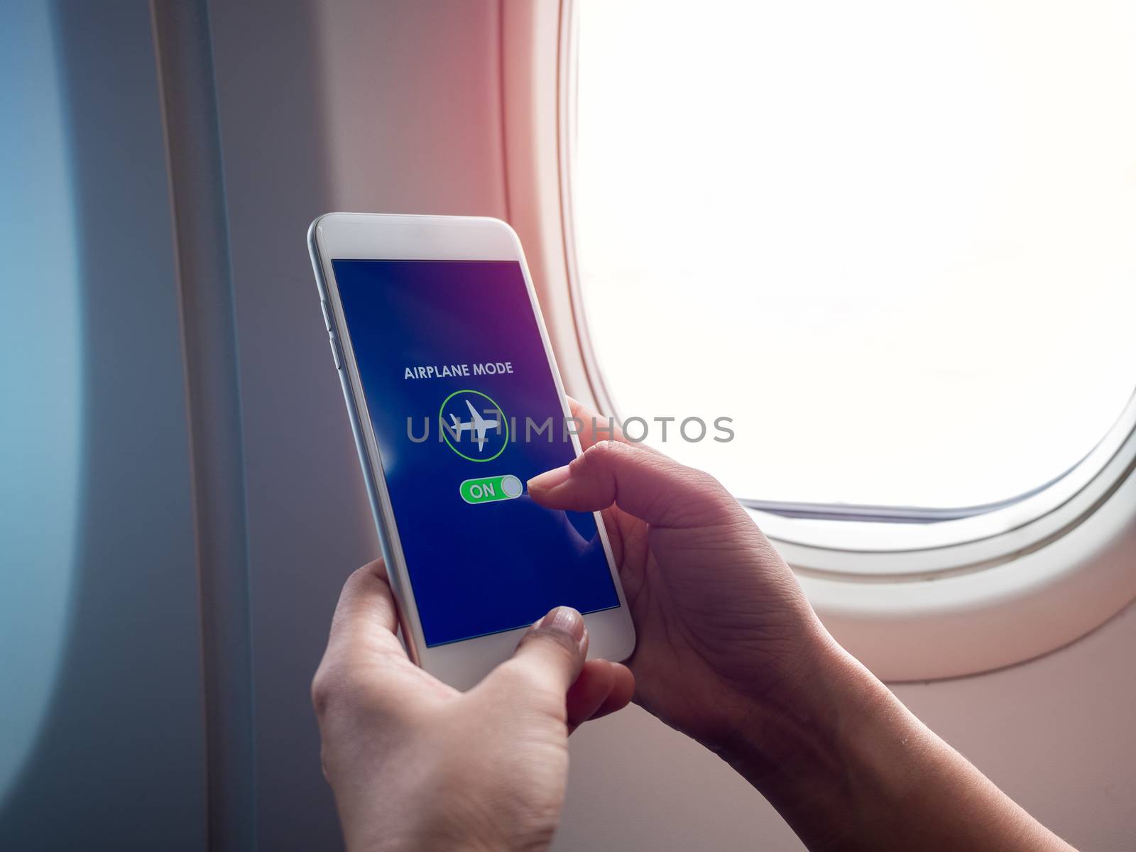 Flight mode concept. Finger sliding on screen for turned on airplane mode near the window on the airplane with copy space.