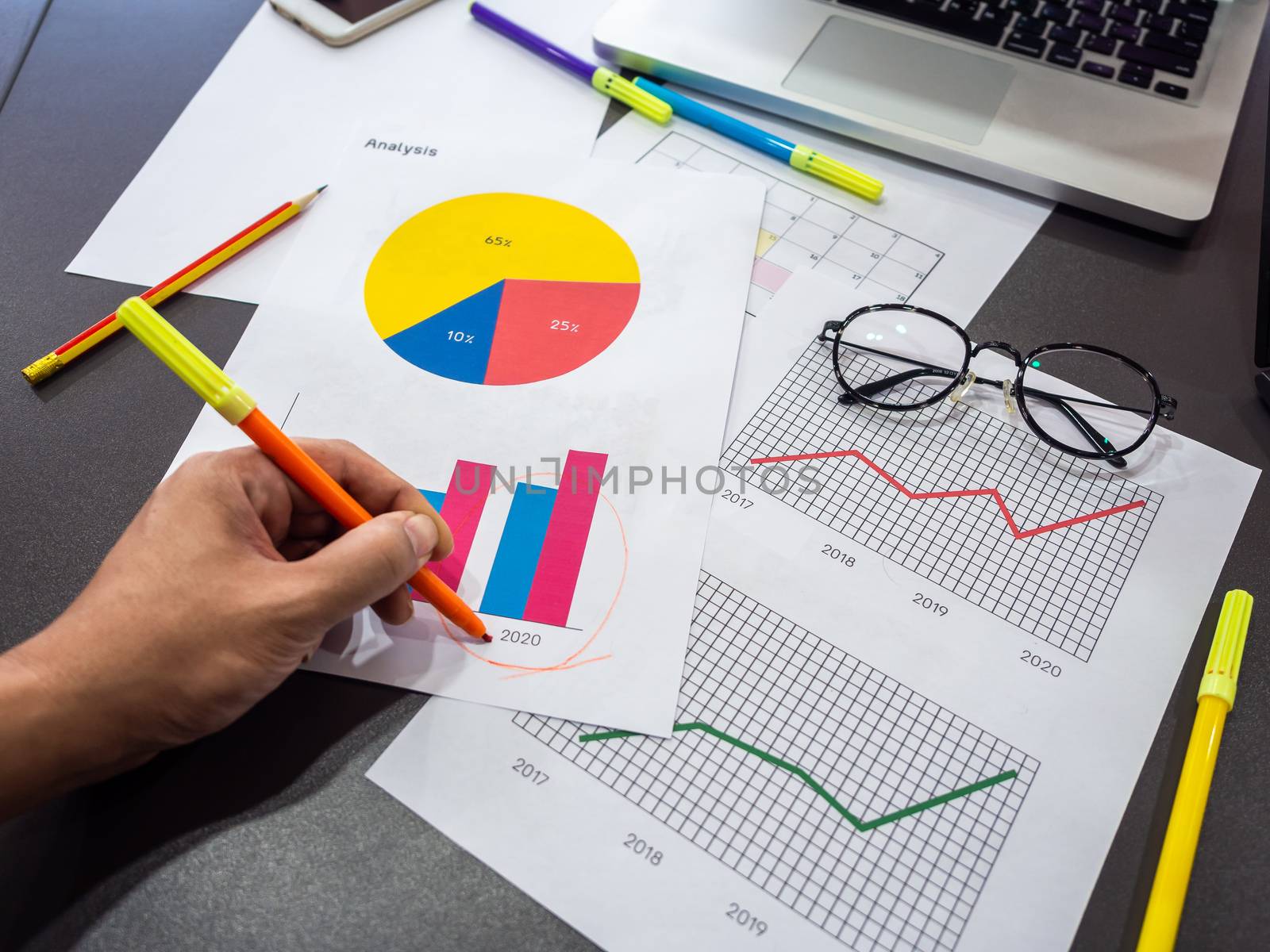 Business goal concept. Hand draw circle around 2020 on diagrams graphs with highlighter pen and business accessory, smartphone, laptop computer, glasses and on table.