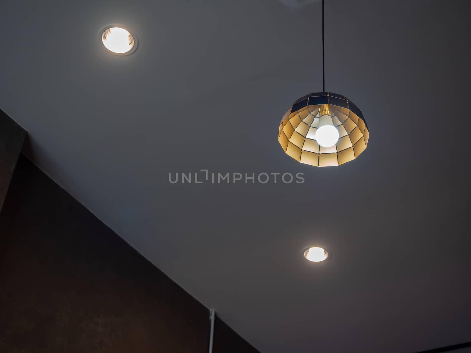 Modern ceiling light hanging from ceiling with downlight in dark room.