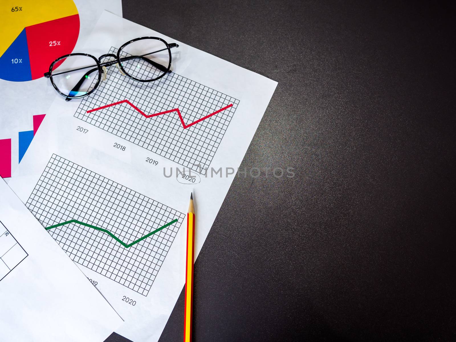 Business goal concept. Top view of business accessory, diagrams graphs, pencil and glasses on dark table with copy space.