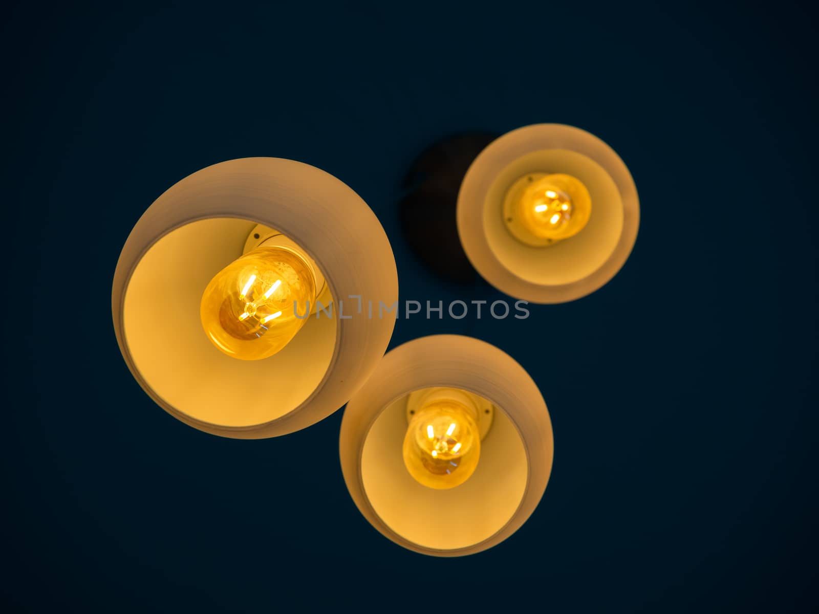 Three round modern ceiling lights hanging from ceiling from bottom view in dark blue room.