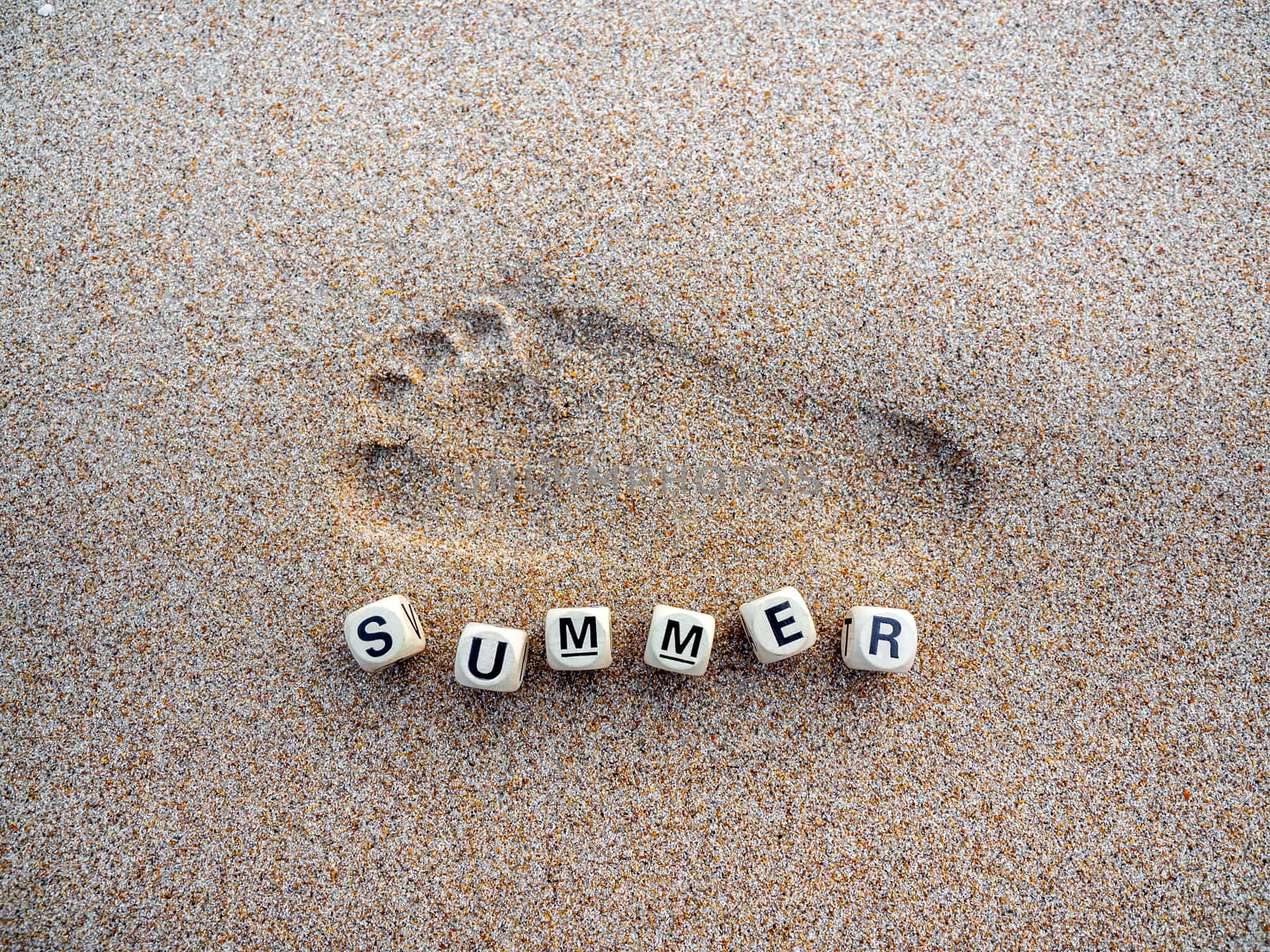 Children footprint and text "summer" on wooden cube blocks on sand on the beach, summer concept.