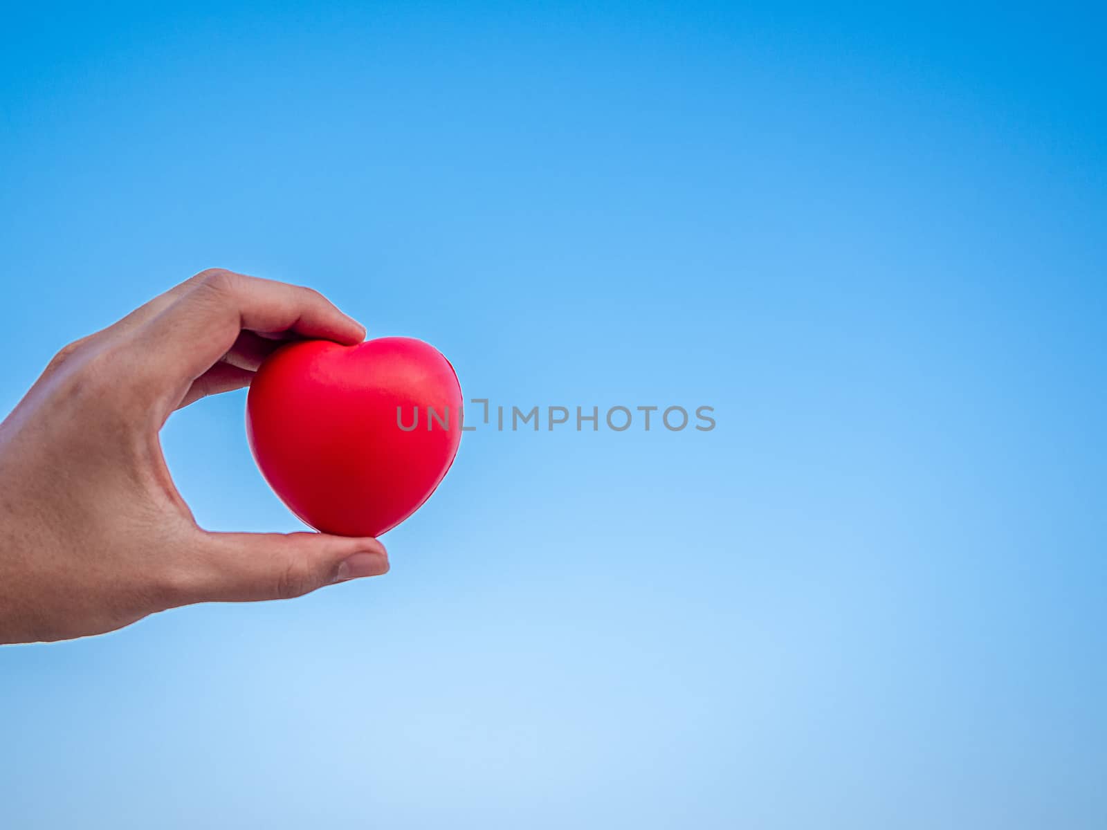 Red heart in hand on blue sky background with copy space, love, peace and giving concept.